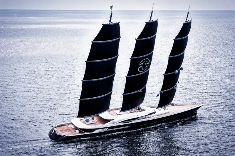 Black Pearl under three black square-rigged sails, aerial view from the stern quarter showing the teak decks and pool