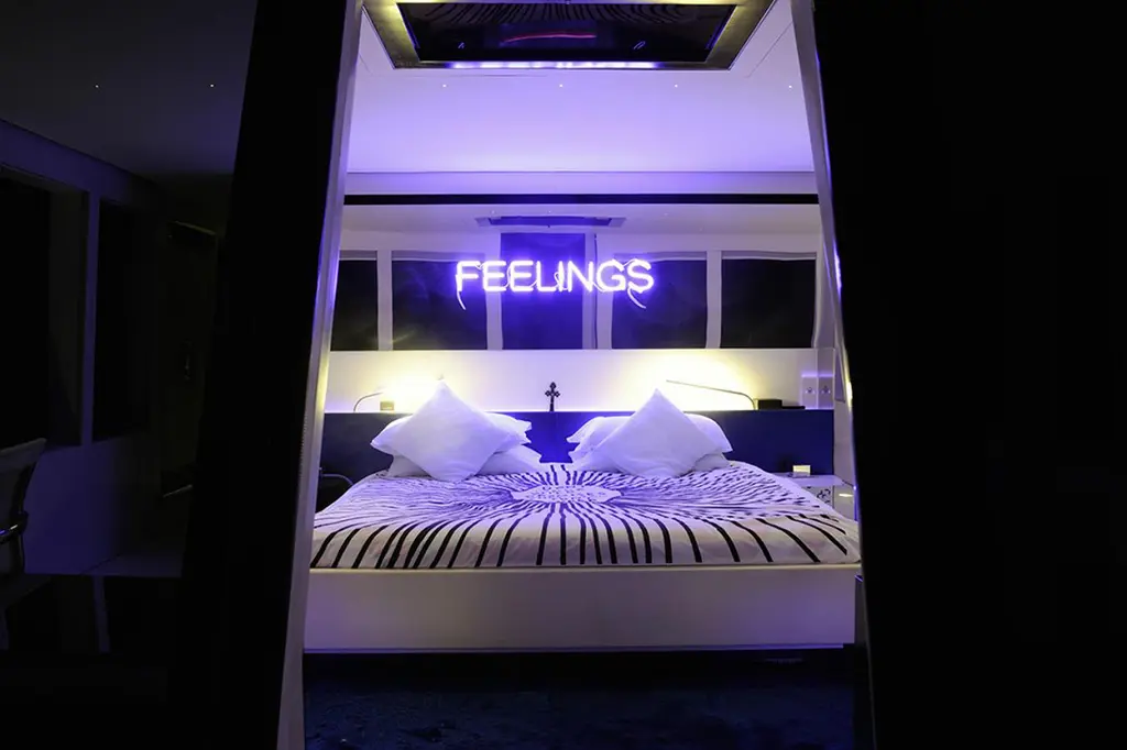 The owner's bed at night seen through a doorway, lit by the purple FEELINGS neon