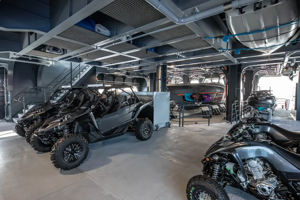 The garage below deck with black side-by-side ATVs and quad bikes on a grey floor and tenders stowed behind