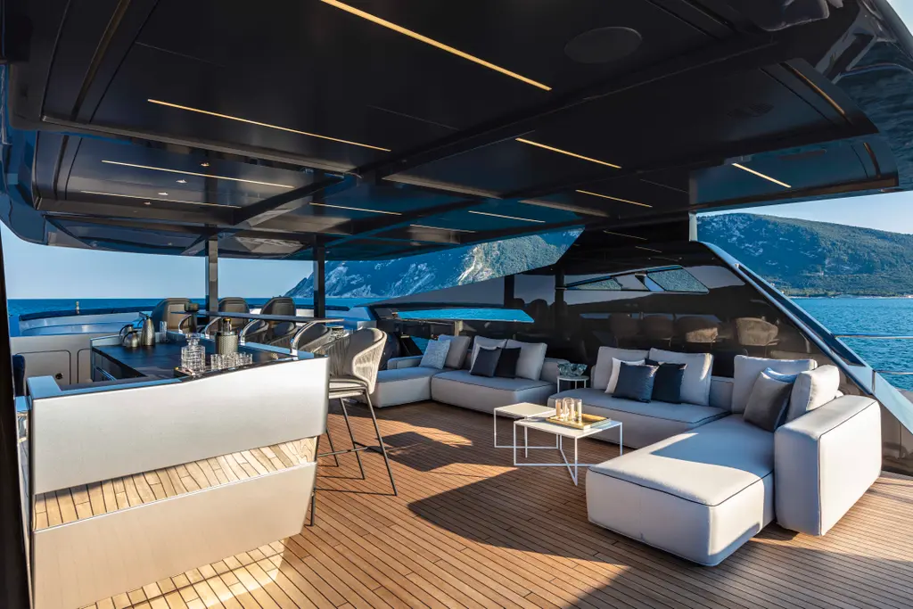 Cockpit lounge under the hardtop bimini, with white sofas, a low table and wide side openings to the sea