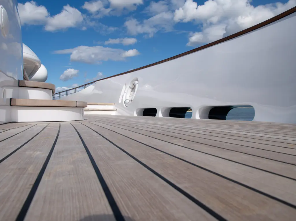 A wide teak side deck curving along the white superstructure under a blue sky