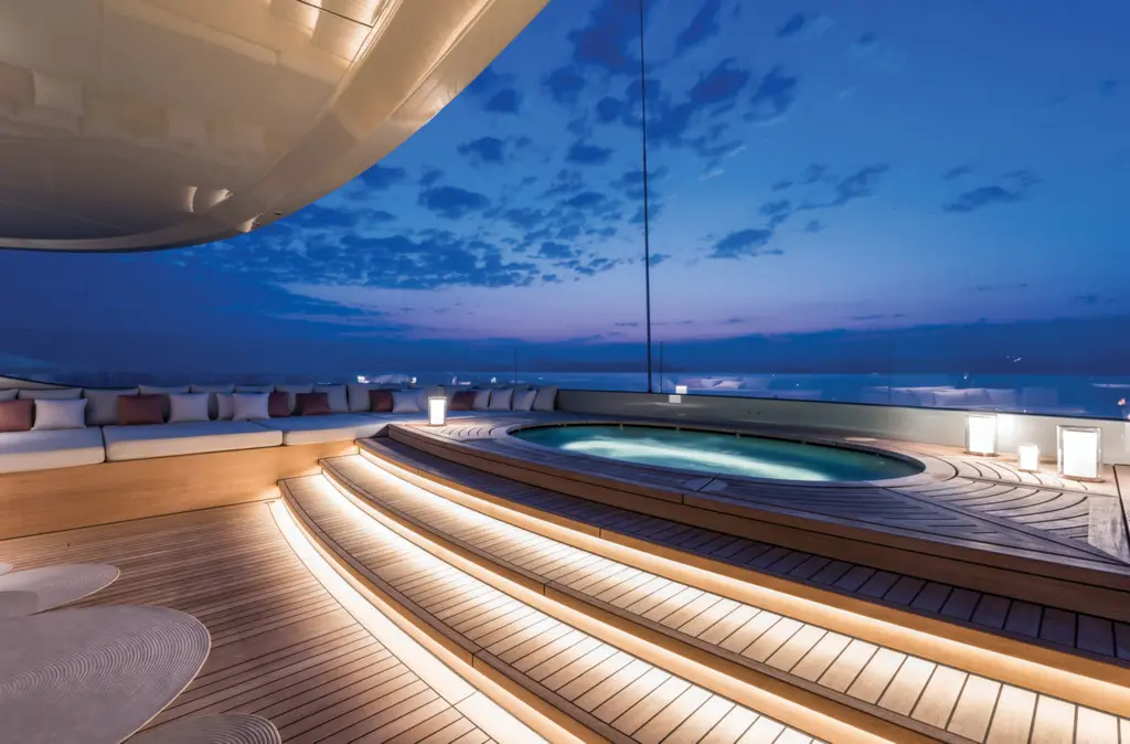 A round Jacuzzi on the sundeck at dusk, set in wooden steps under the overhang of the hardtop