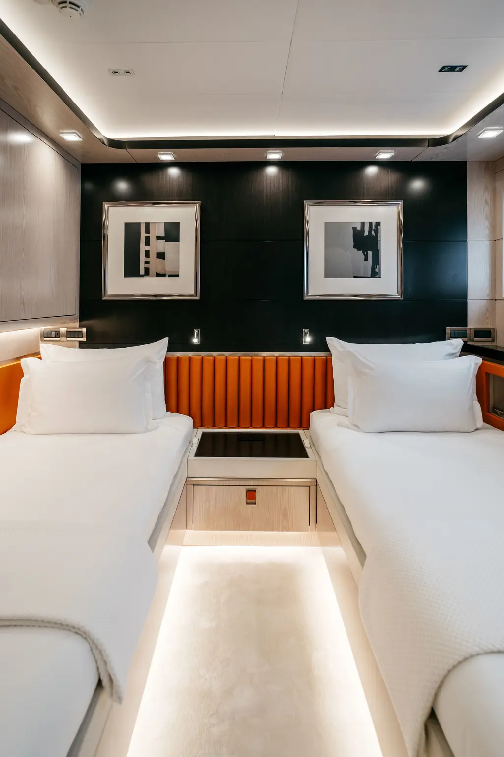 Twin guest cabin with two single beds, an orange upholstered headboard and framed prints