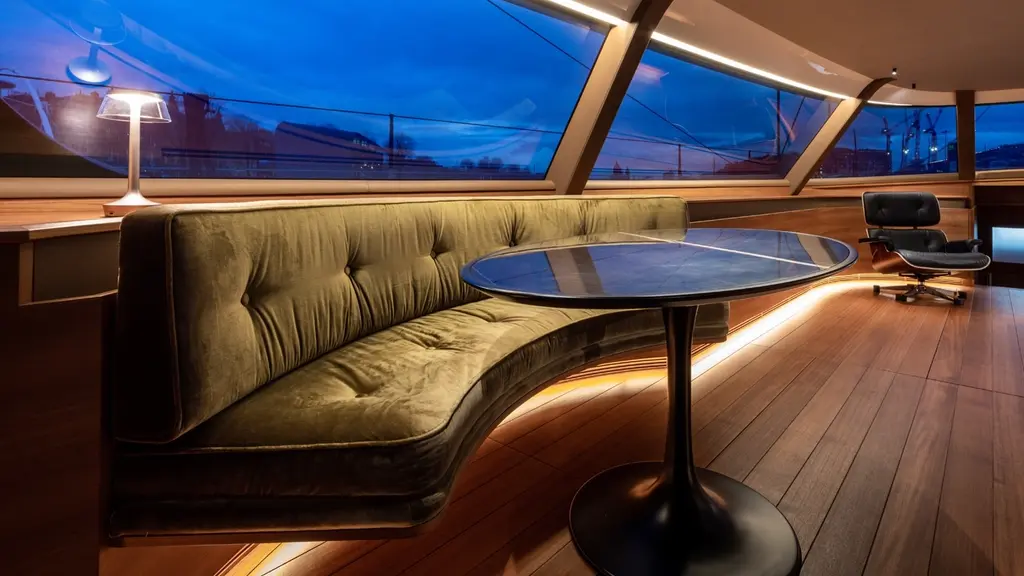 Deck saloon with a curved olive sofa around a round table, panoramic windows and a leather lounge chair