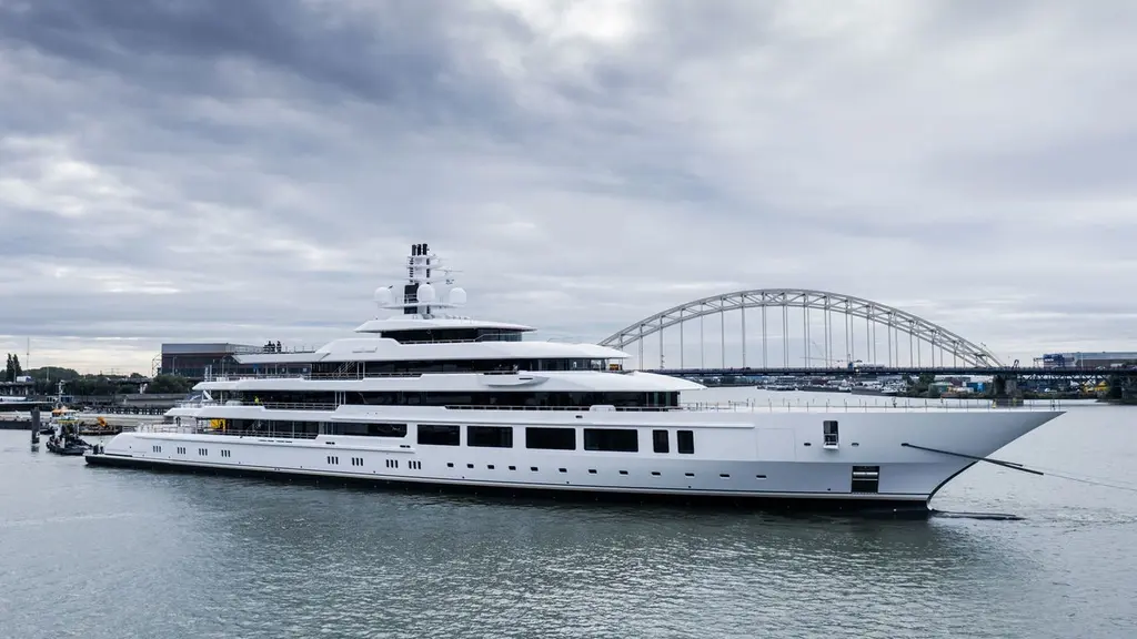 Infinity on a river in starboard profile, with a steel arch bridge behind and an overcast sky
