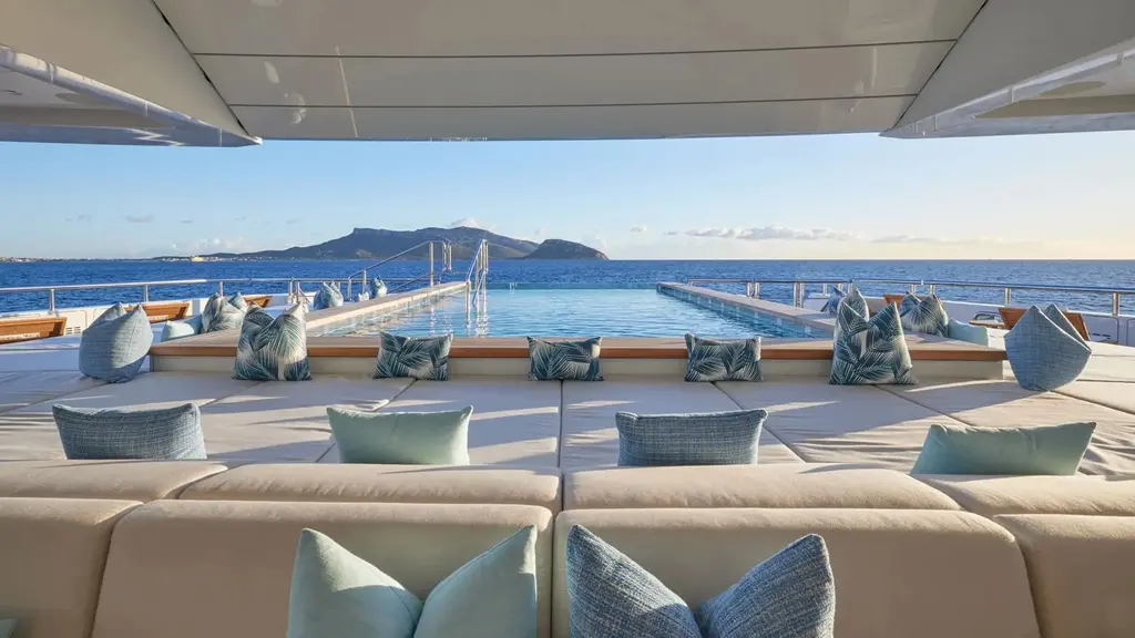 Long swimming pool seen from a sofa with blue cushions, sea and an island behind