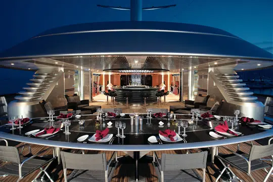 Aft deck dining table laid for dinner at dusk, the main saloon lit up behind