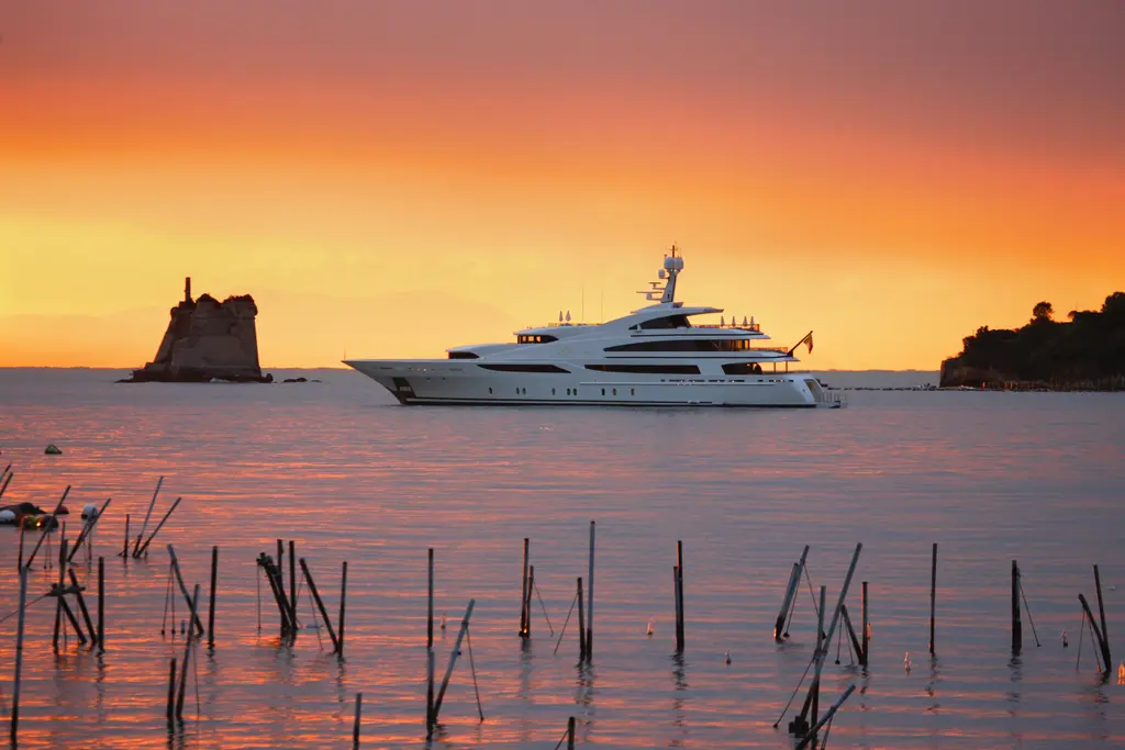 The yacht offshore at sunset, orange sky, a stone tower on a rock to the left