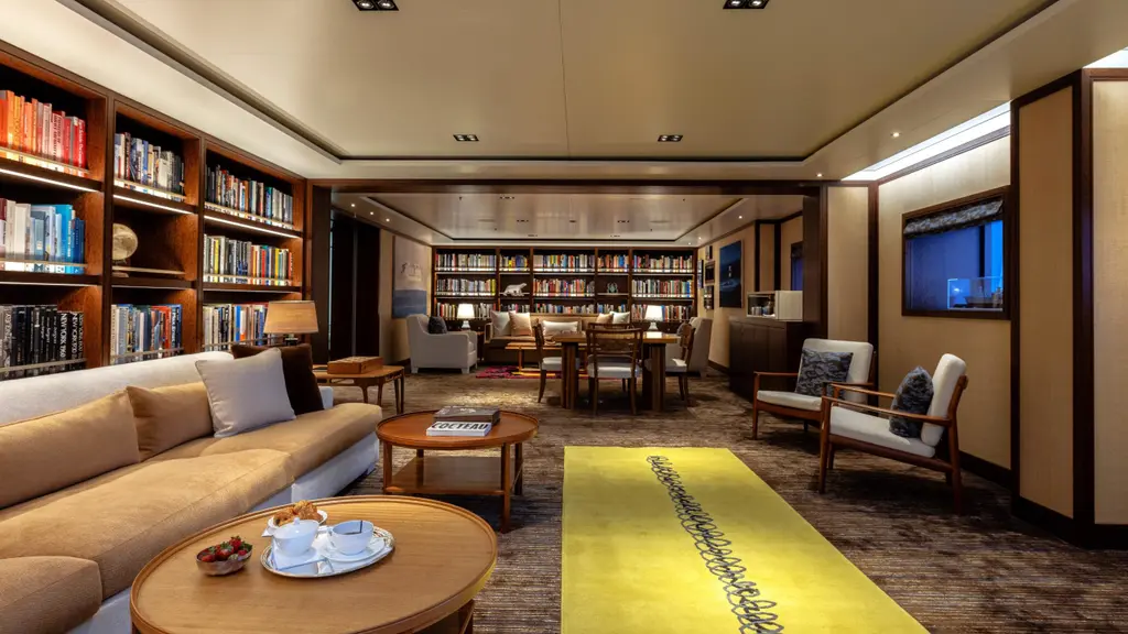 Owner's lounge with floor-to-ceiling bookshelves, sofas, a television on the wall and a yellow rug