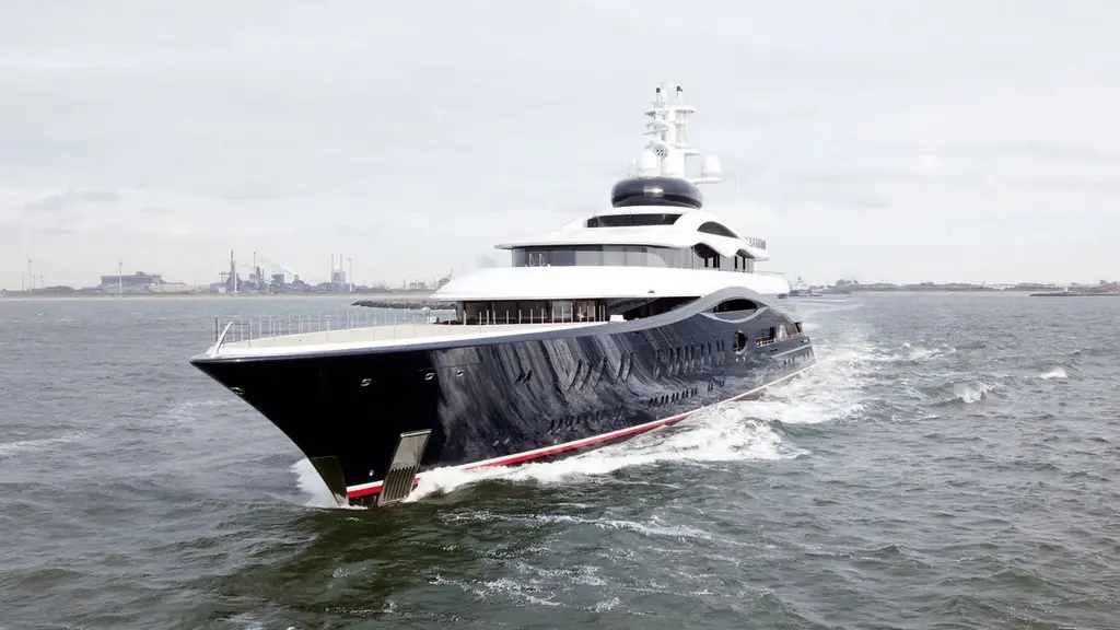Launchpad's raked dark blue bow cutting through grey water near an industrial coastline