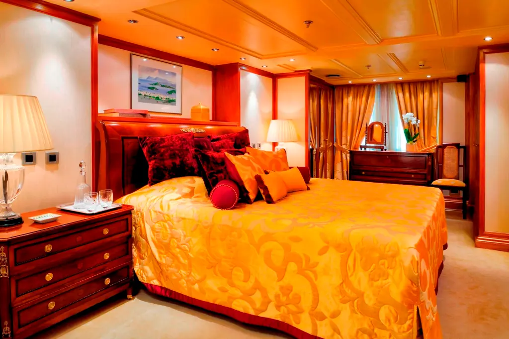 Guest stateroom with a double bed under a gold damask cover and wood panelling