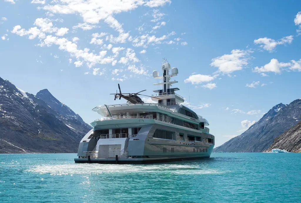 Cloudbreak seen from astern in a fjord, with a helicopter parked on her helideck and mountains on both sides