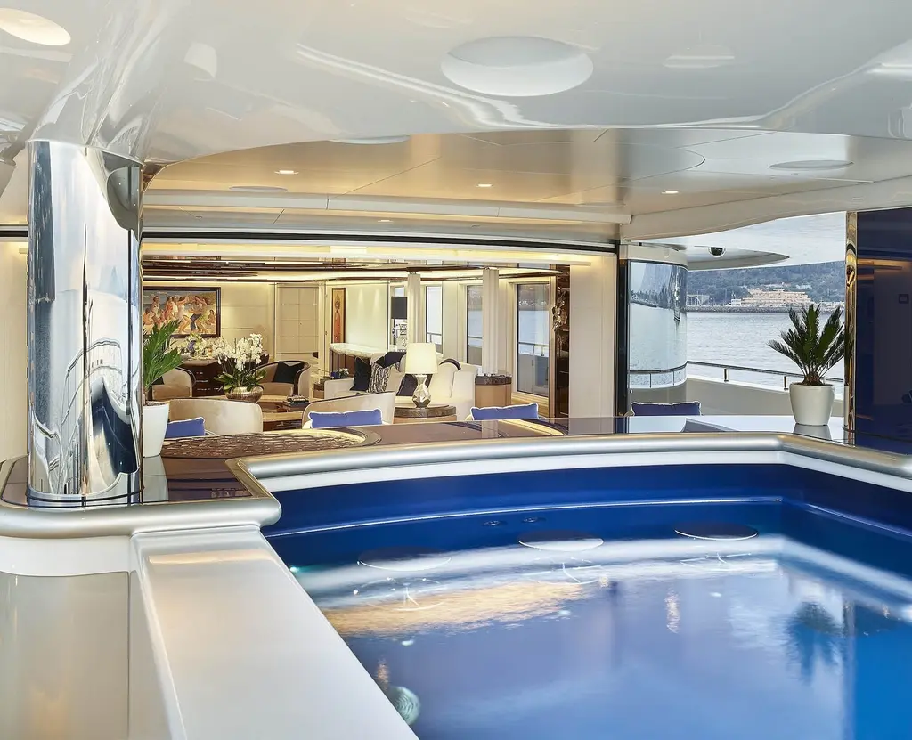 Blue-tiled pool in the foreground with a lounge and dining area behind it and the sea through the side opening