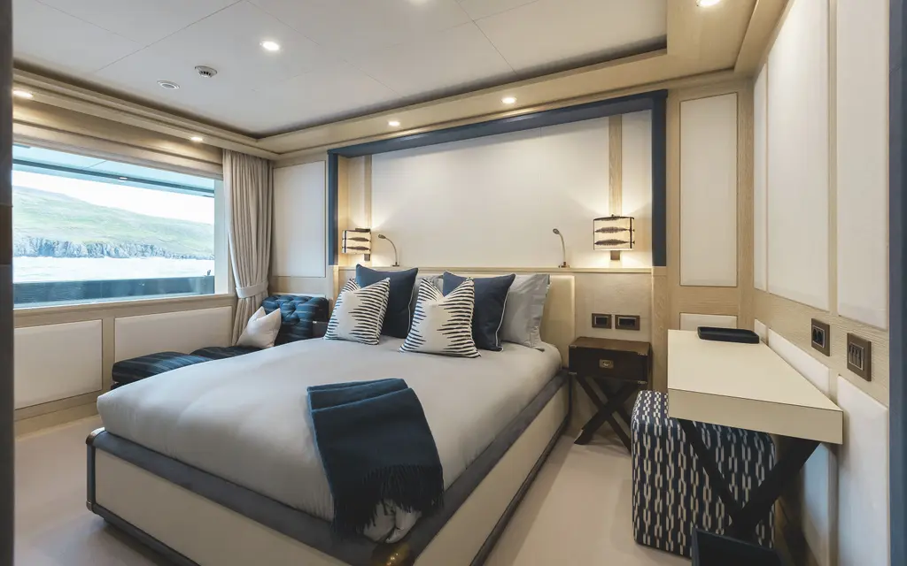 A guest cabin in pale oak and cream with a double bed, a desk and a large window