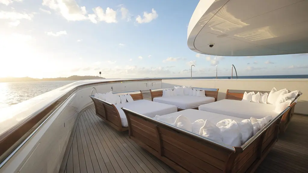 Teak-framed daybeds with white cushions on deck at sunset