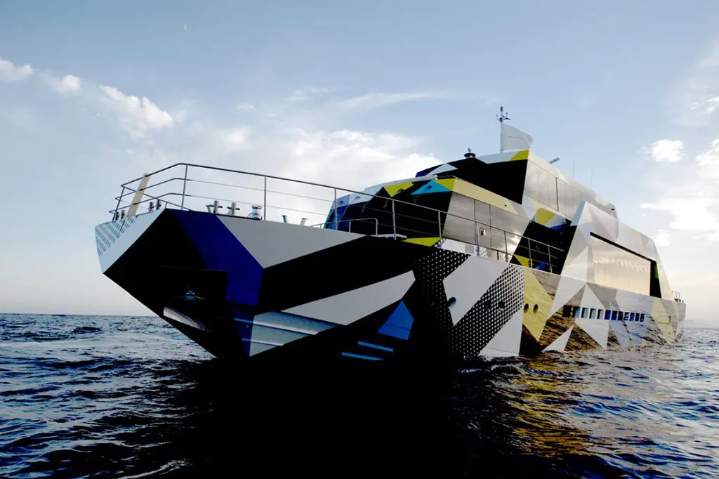Guilty seen low from the bow at sea, her blunt cut-off bow and hull covered in black, white, blue and yellow geometric camouflage