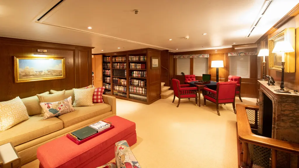 Wood-panelled saloon with a sofa, a red ottoman, bookshelves and a card table