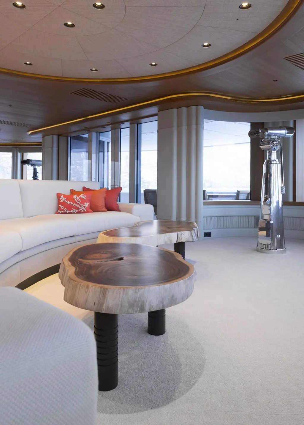 A lounge with a curved white sofa, orange cushions and a coffee table made from a slab of wood, with windows behind