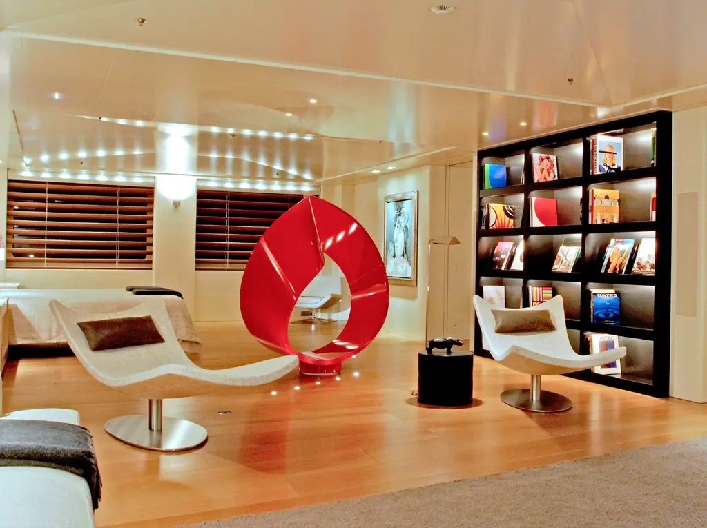 A lounge with white loungers, a red sculptural chair and a tall black bookcase