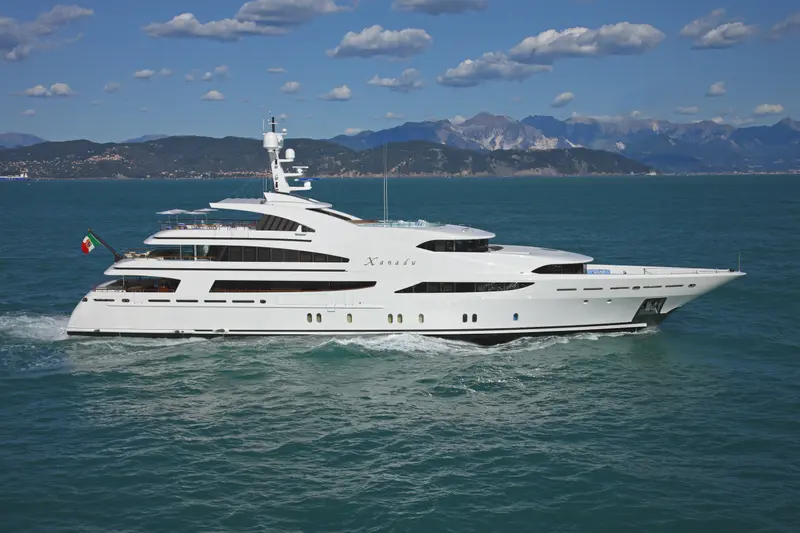 White 60 m motor yacht underway at sea, side profile, mountains behind