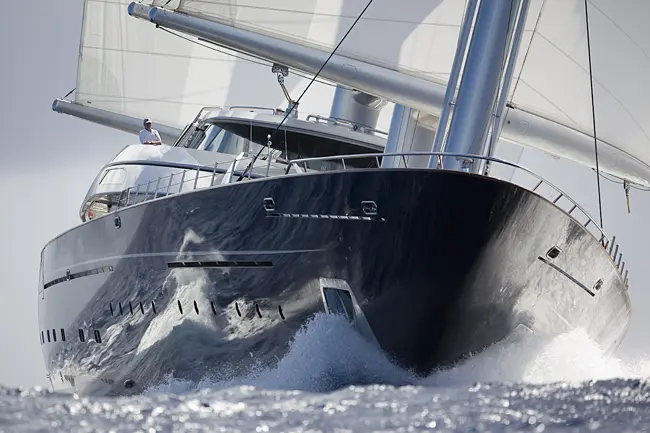 Close view of Maltese Falcon's dark hull and bow cutting through a wave, the foremast and yards above