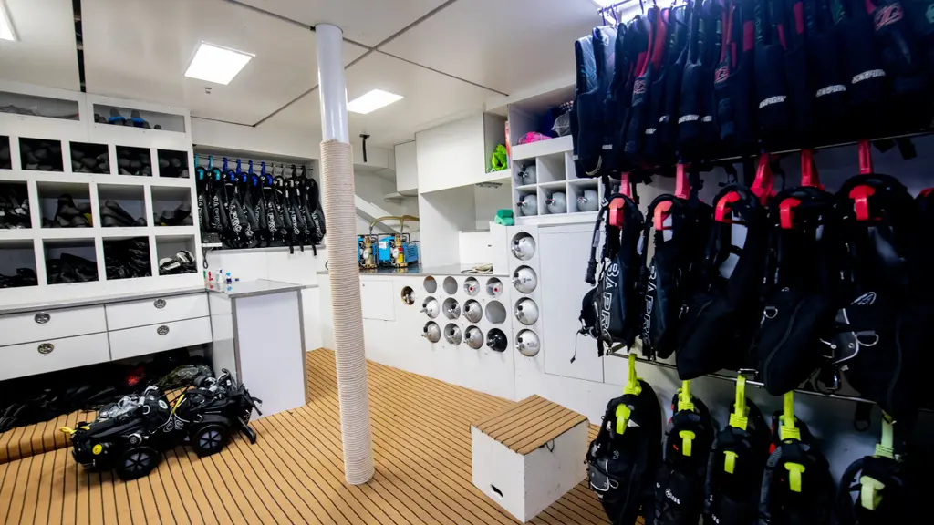 Dive room with racks of buoyancy jackets and wetsuits, scuba cylinders in wall racks and underwater scooters on the floor
