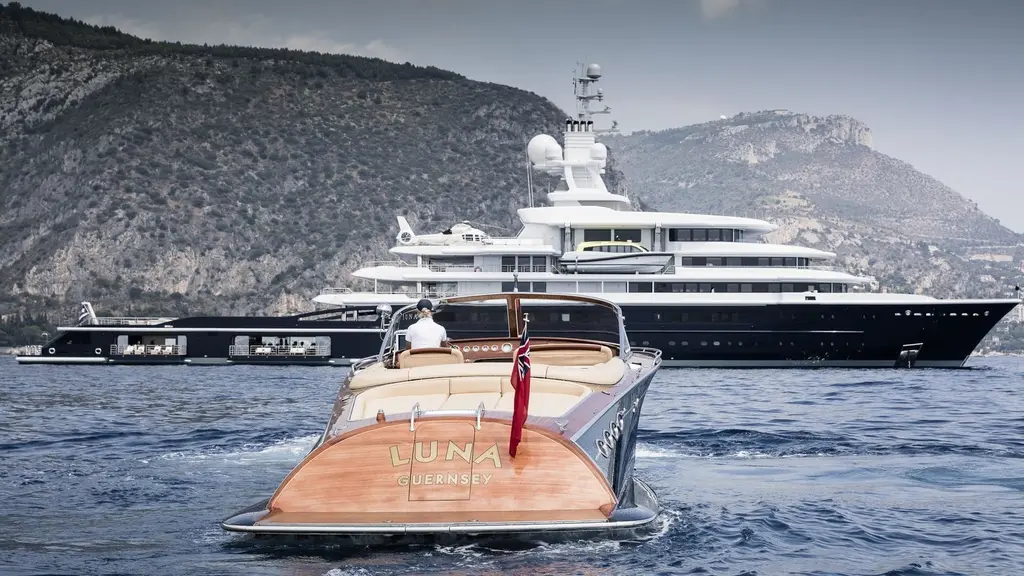 A wooden tender named Luna heading out from the yacht at anchor below a rocky coastline