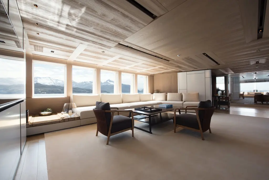 A lounge with long cream sofas, wooden armchairs and a row of large windows looking onto snowy mountains
