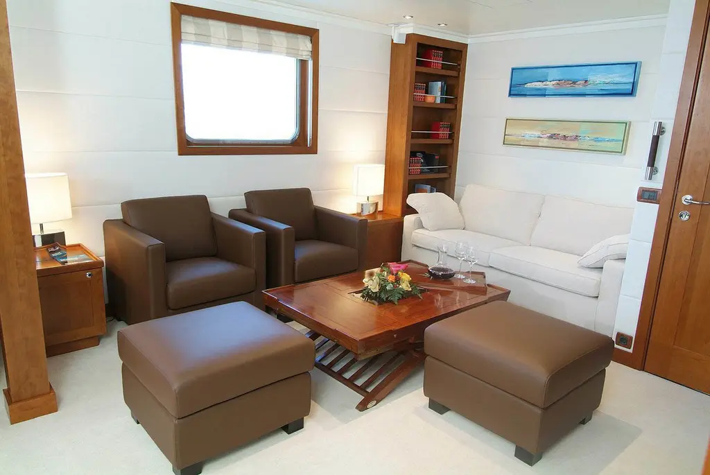 Small lounge with leather armchairs, a cream sofa and a bookcase, before the 2021 refit