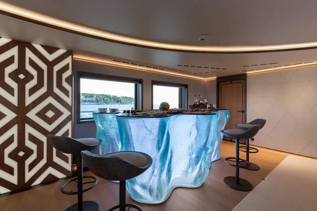 Bar with a translucent sculpted counter, black stools and a geometric wall panel