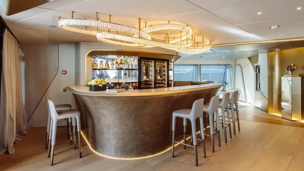 Curved bar with white stools under ring-shaped chandeliers