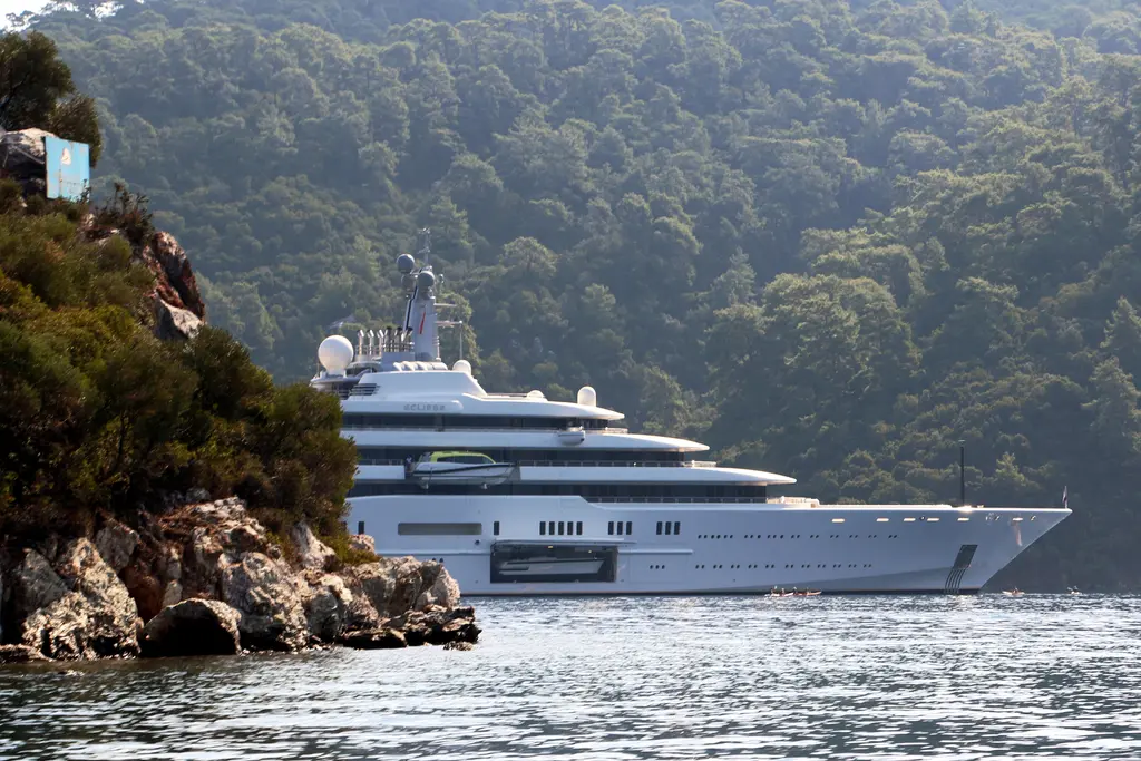 Eclipse at anchor in a bay with wooded hills and rocks in the foreground