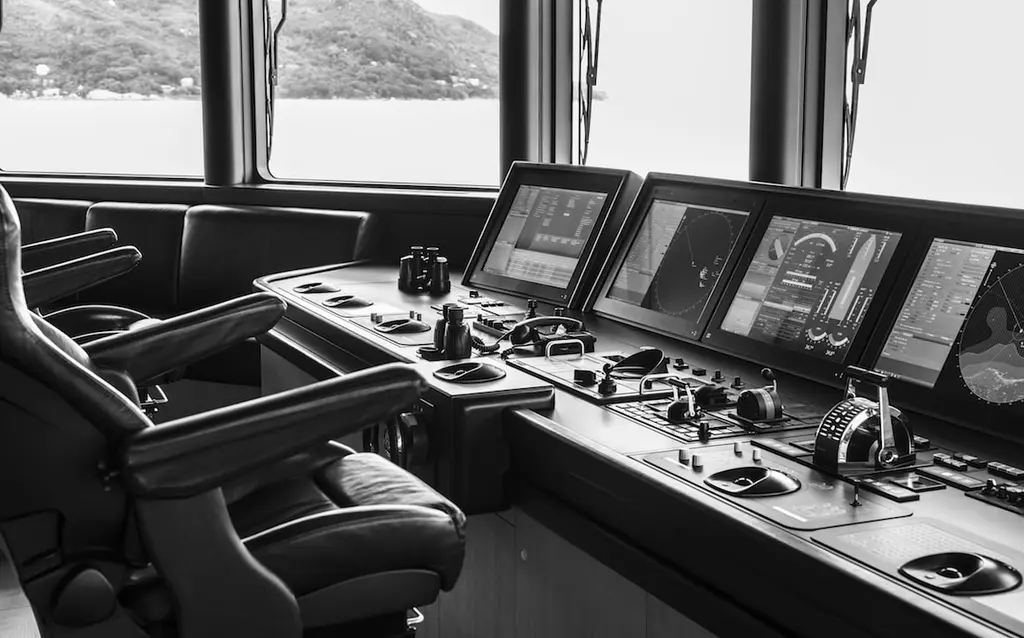 Black-and-white view of the bridge, with helm chairs and a console of screens facing the windows