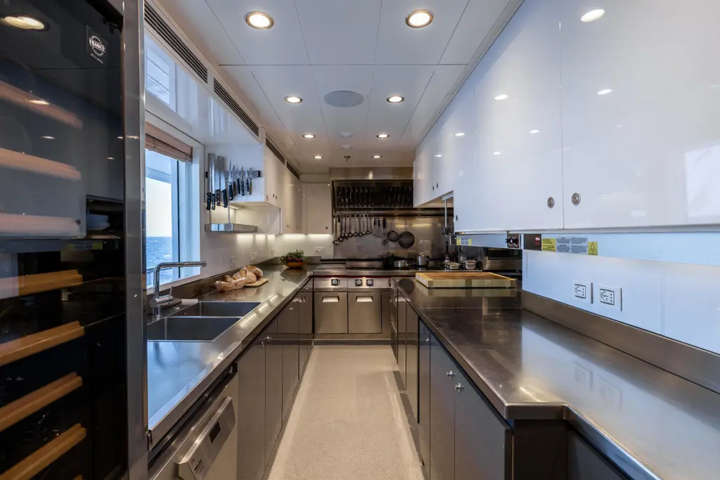 Galley with stainless-steel worktops, ovens, hanging pans and a wine fridge