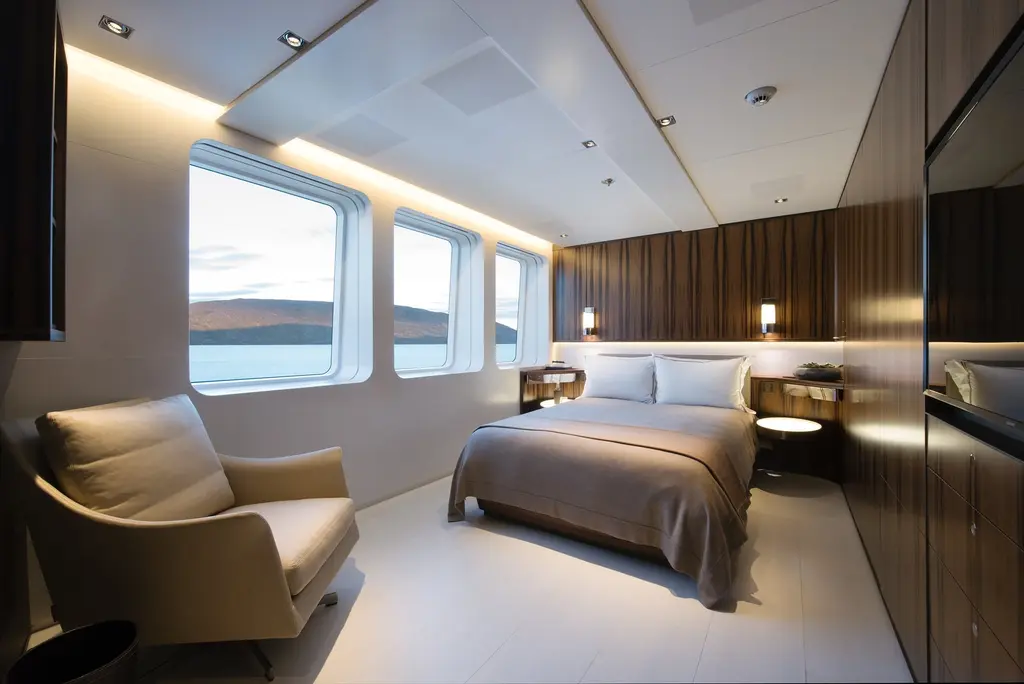 A guest cabin with a double bed, an armchair and a row of windows onto the water