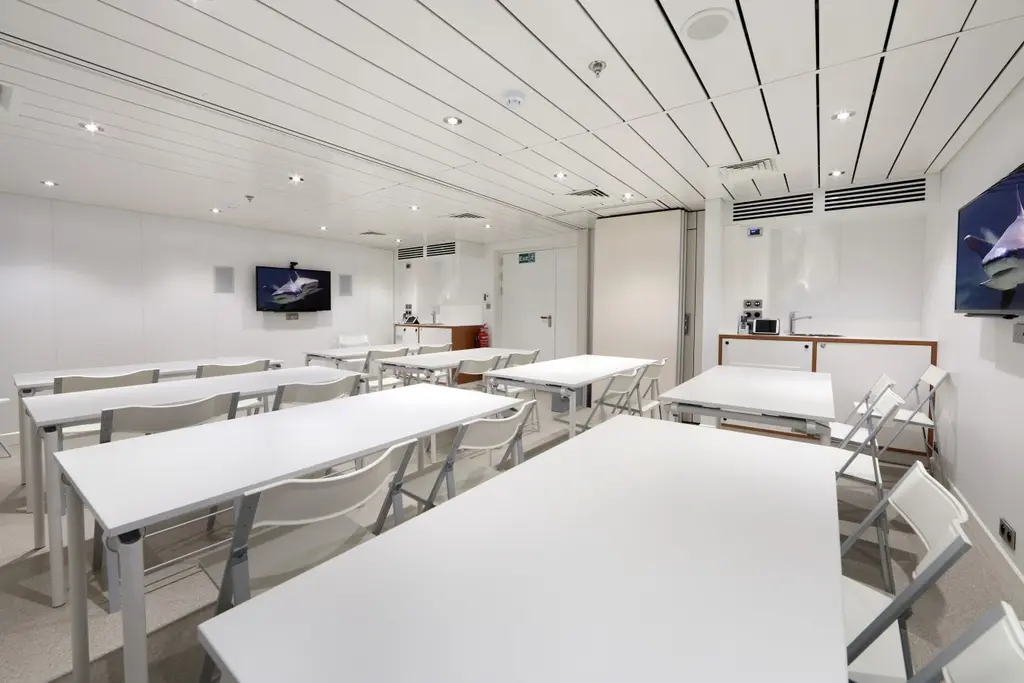 Plain white multipurpose room with rows of tables and folding chairs and wall screens, set up as a classroom