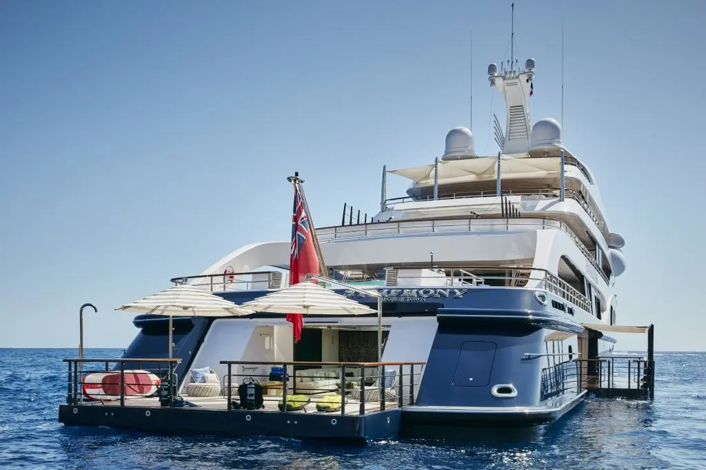 Symphony's stern with fold-down platforms, parasols and the red ensign; the transom reads Symphony, George Town