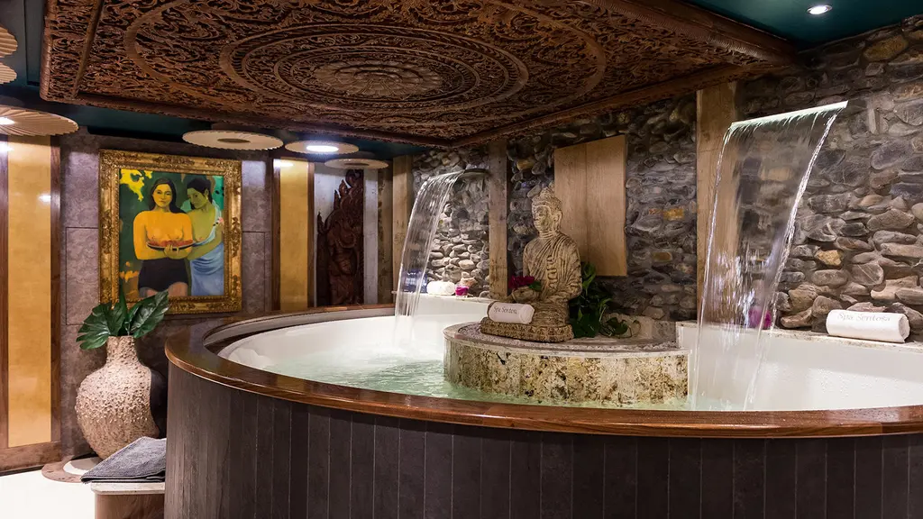 Balinese-style spa with a round spa pool, a stone wall with water features and carved wooden panels