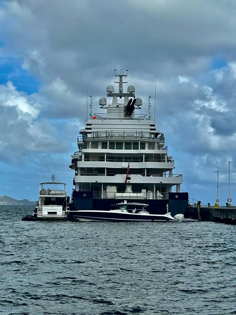 Stern view of Multiverse at a pier under cloudy skies, with two tenders moored behind her
