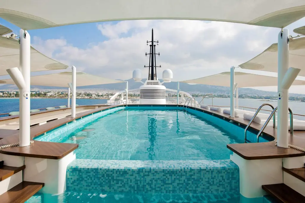 Mosaic-lined sundeck pool under white sail shades, mast in the background