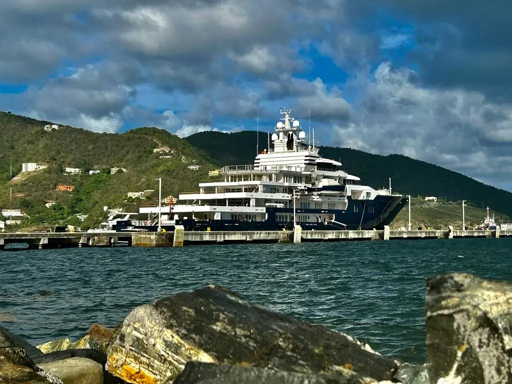 Multiverse moored at a concrete pier below green hills, starboard side