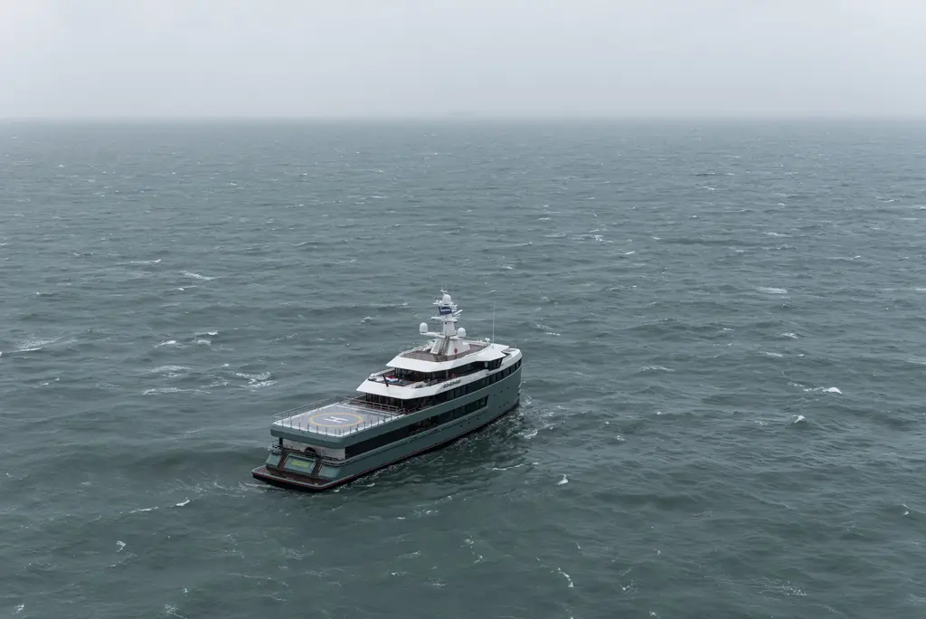 Anawa seen from astern and high above, alone on a grey sea, with the square helideck over the stern and the superstructure forward