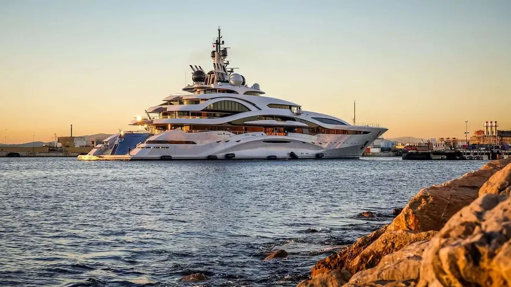 Al Lusail moored in a harbour at sunset, seen across the water from rocks in the foreground