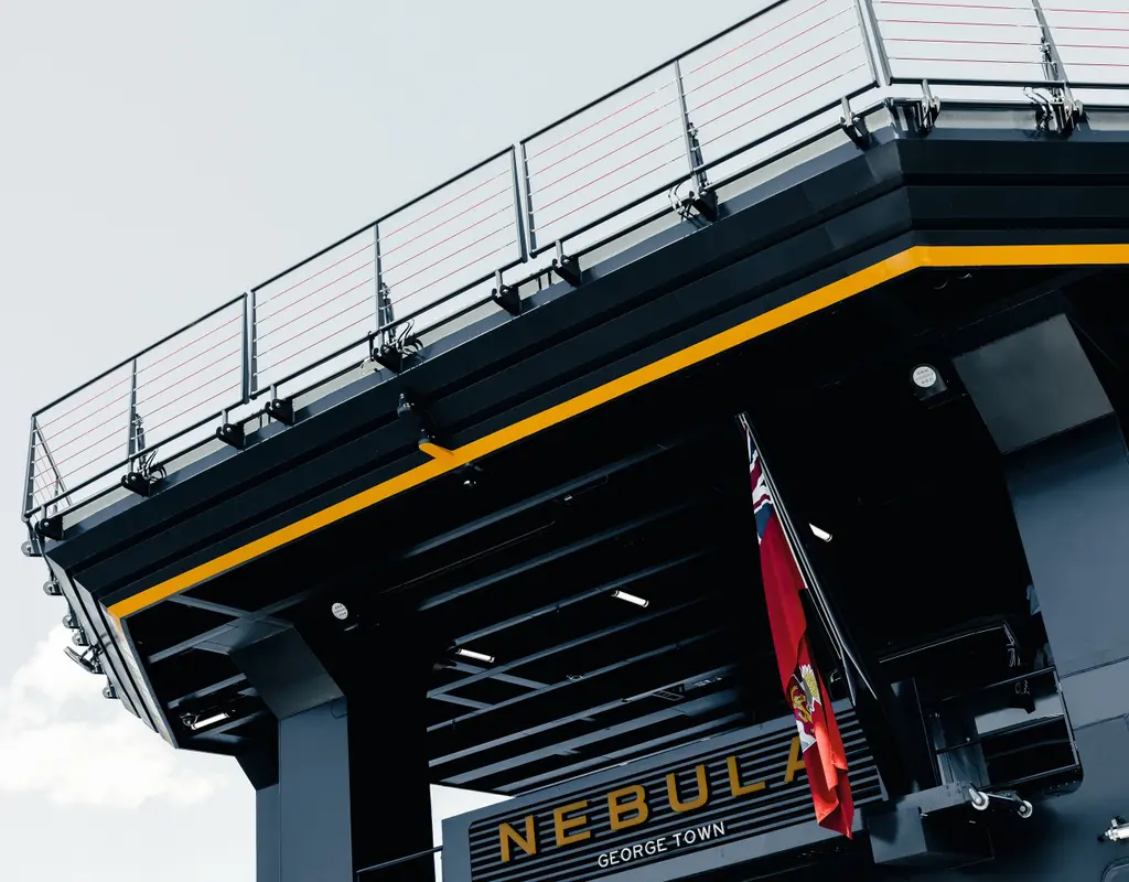 Low view of Nebula's stern under the overhanging helideck, with the name NEBULA, the port of registry George Town and a red ensign