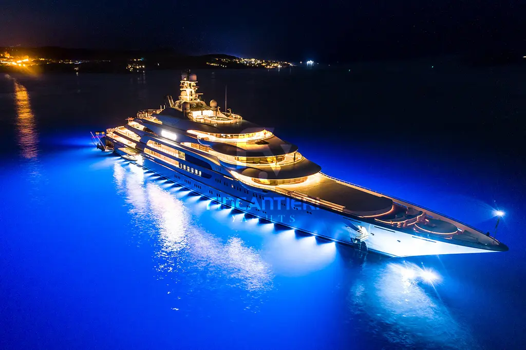 Ocean Victory lit at night with blue underwater lights, seen from the bow quarter