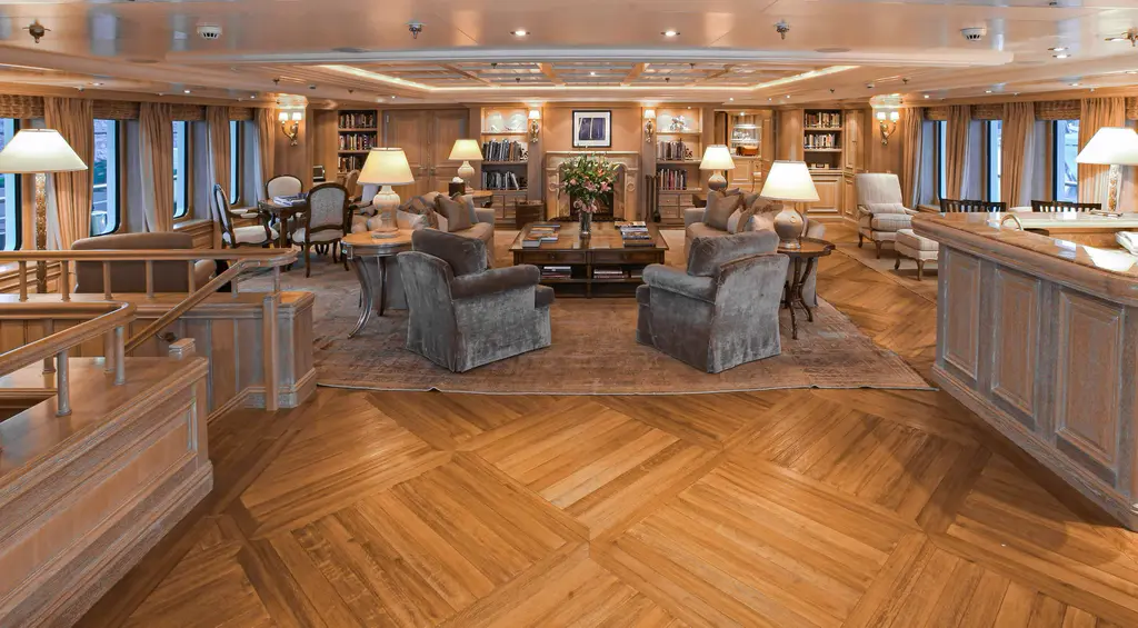 Large salon with herringbone parquet, bookcases, grey armchairs and a bar counter