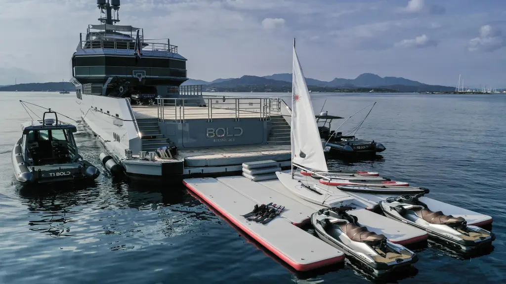 A floating dock at the stern with jet skis and a sailing dinghy, and a RIB tender alongside
