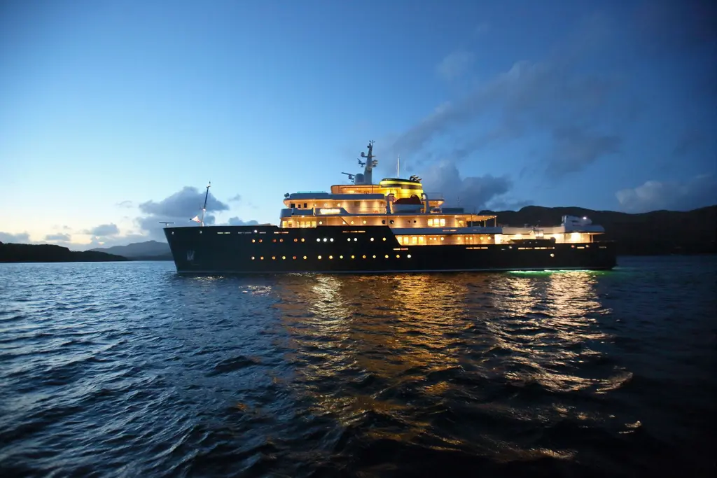 Yersin at dusk with all decks lit, reflected in the water