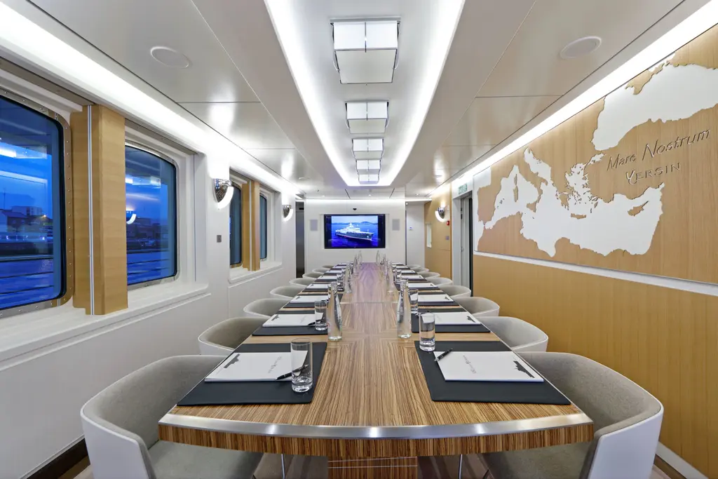 Long dining or conference table set with notepads, with a Mediterranean map and the words Mare Nostrum and Yersin carved into the wooden wall