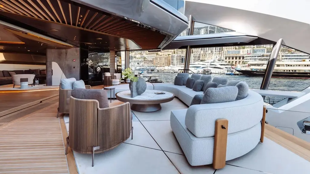 Covered outdoor lounge with curved grey sofas, a round table and armchairs, open to the harbour